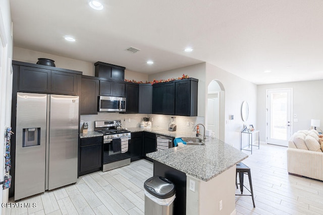 kitchen featuring sink, a kitchen bar, backsplash, stainless steel appliances, and light stone counters