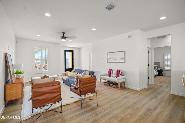 living room with baseboards, a ceiling fan, visible vents, and light wood-style flooring