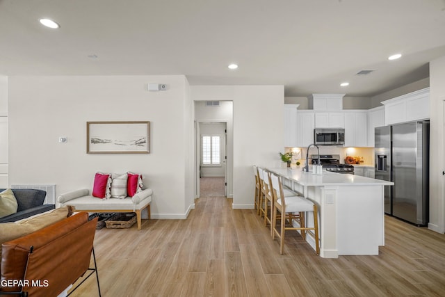 kitchen featuring a kitchen breakfast bar, open floor plan, light wood finished floors, light countertops, and appliances with stainless steel finishes