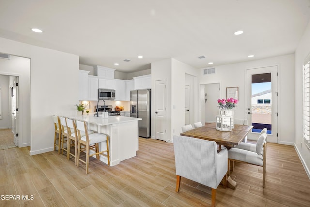 kitchen featuring light wood-style floors, a breakfast bar area, white cabinets, a peninsula, and appliances with stainless steel finishes