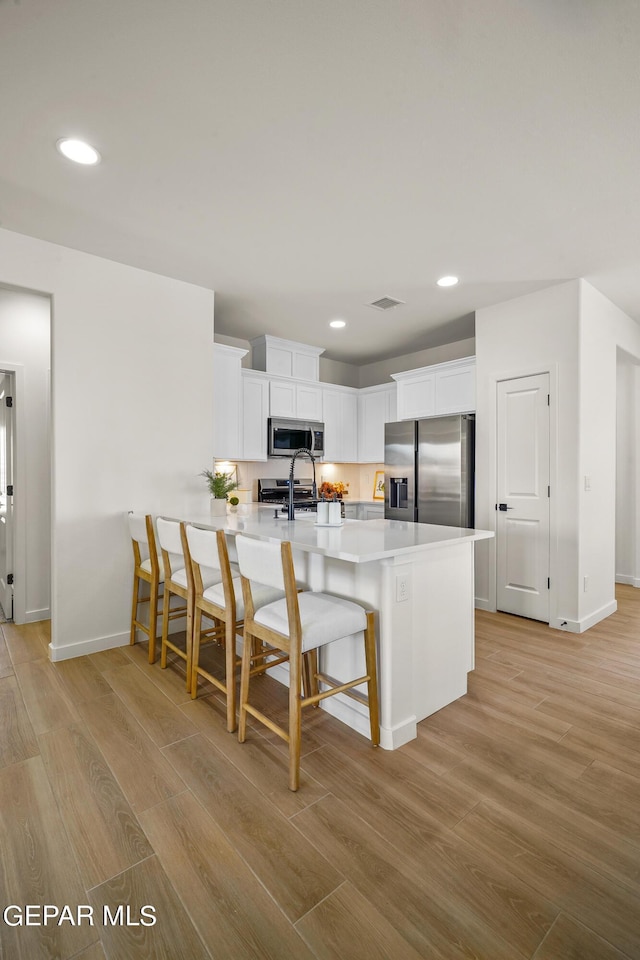kitchen featuring baseboards, white cabinetry, stainless steel appliances, and light wood-style flooring