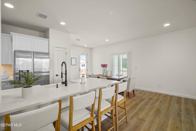 kitchen featuring light wood finished floors, stainless steel fridge, visible vents, recessed lighting, and white cabinetry