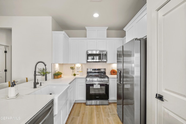 kitchen with light countertops, a sink, light wood-type flooring, appliances with stainless steel finishes, and white cabinetry