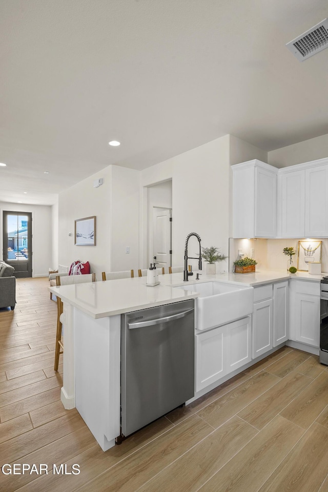 kitchen with a sink, open floor plan, light wood-style floors, dishwasher, and visible vents