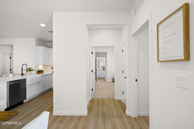 corridor with baseboards, light wood-style floors, visible vents, and a sink