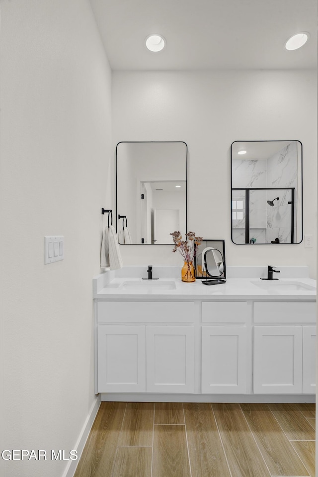 bathroom with double vanity, a shower, wood finished floors, and a sink