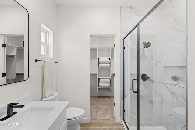 full bath featuring a walk in closet, a shower stall, toilet, and vanity