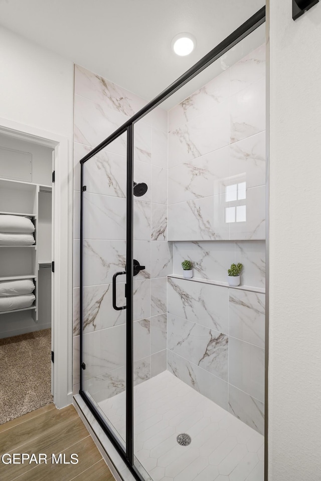 full bath with wood finished floors, a walk in closet, and a stall shower