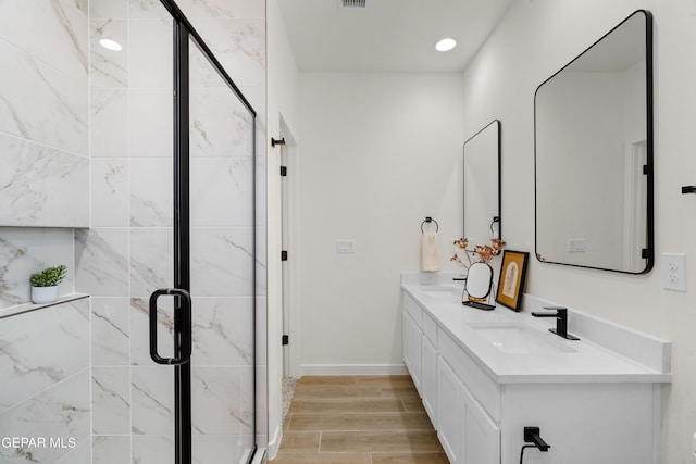 full bath with wood finished floors, a sink, a marble finish shower, double vanity, and visible vents
