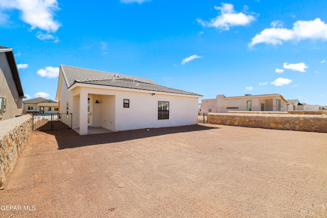 back of house featuring fence, a tiled roof, and stucco siding
