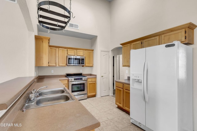 kitchen with light tile patterned flooring, a towering ceiling, stainless steel appliances, light brown cabinets, and sink