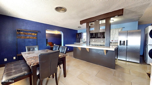 kitchen featuring a textured ceiling, stacked washing maching and dryer, stainless steel refrigerator with ice dispenser, and a breakfast bar area