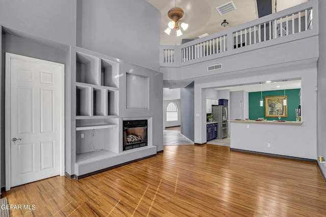 unfurnished living room featuring a towering ceiling, hardwood / wood-style flooring, and ceiling fan