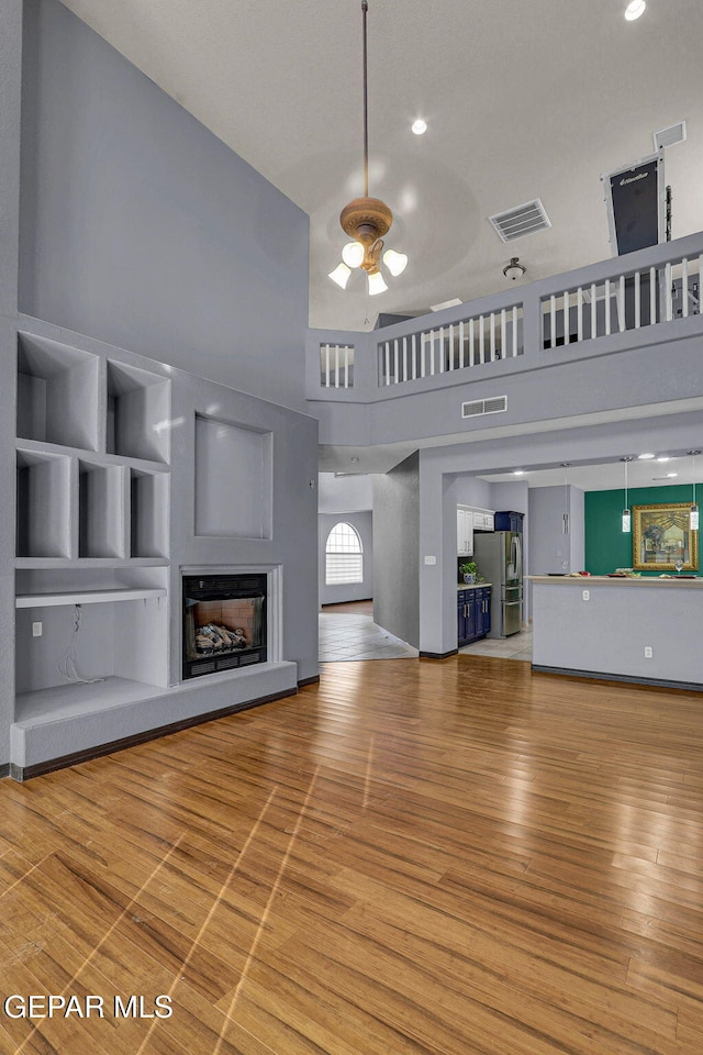 unfurnished living room featuring wood-type flooring, ceiling fan, and a high ceiling