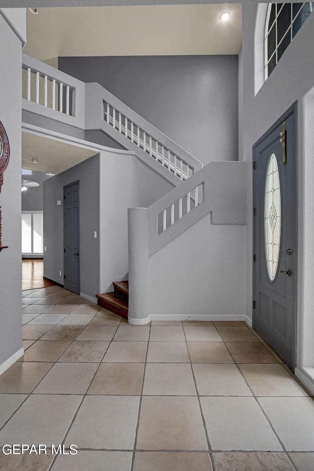 foyer with ceiling fan, plenty of natural light, a towering ceiling, and light tile patterned floors