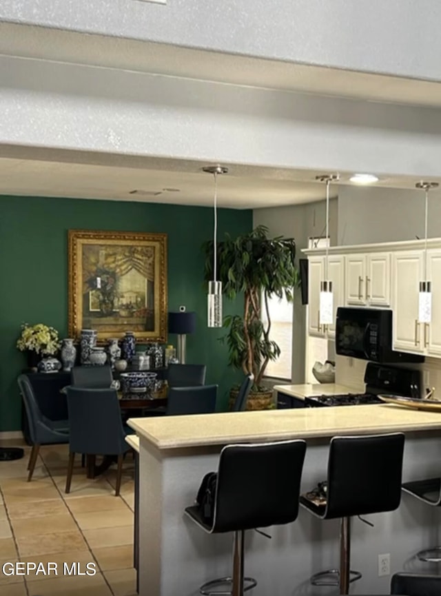 kitchen with pendant lighting, black appliances, a kitchen breakfast bar, white cabinets, and light hardwood / wood-style flooring