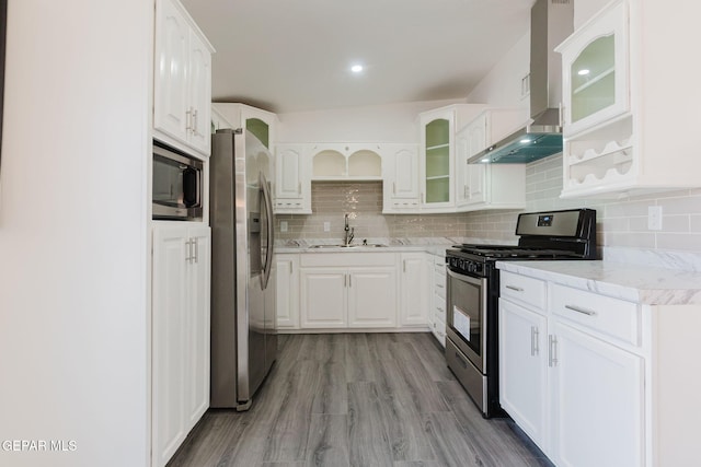 kitchen featuring wall chimney range hood, decorative backsplash, appliances with stainless steel finishes, light hardwood / wood-style floors, and sink