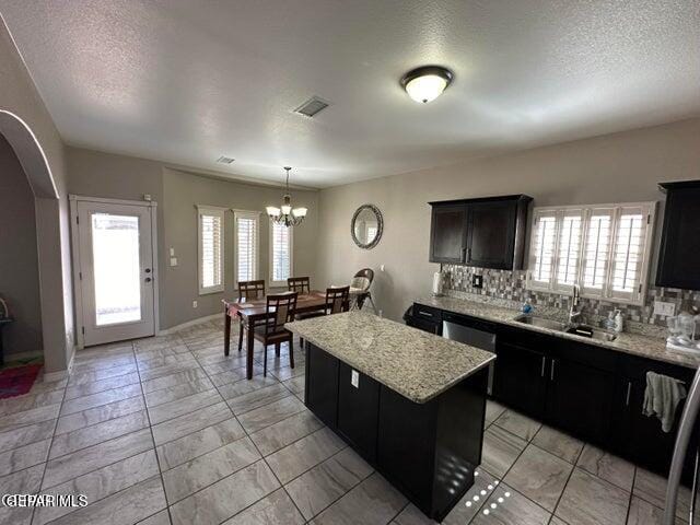 kitchen with sink, a kitchen island, decorative backsplash, and an inviting chandelier