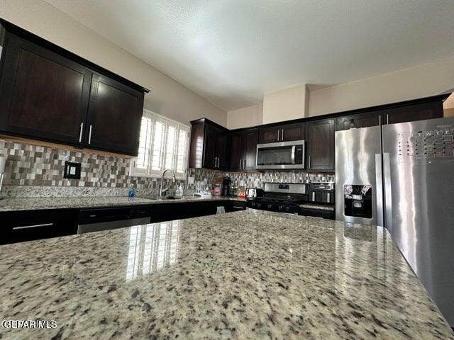 kitchen with dark brown cabinetry, sink, light stone counters, and stainless steel appliances