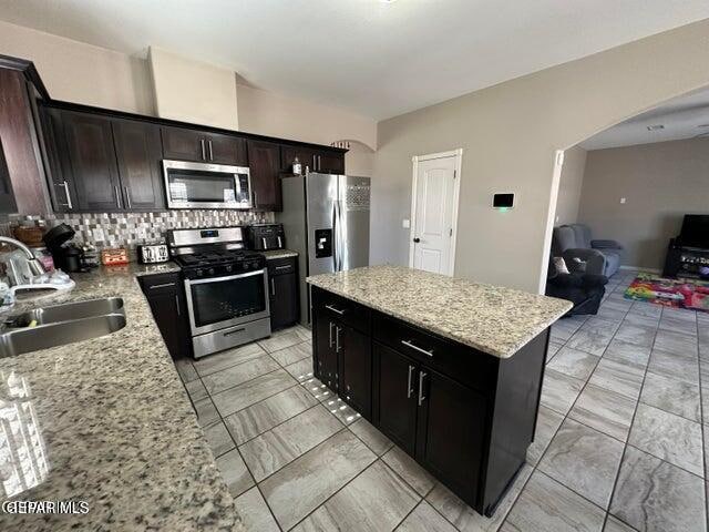 kitchen with backsplash, sink, a center island, appliances with stainless steel finishes, and light stone counters