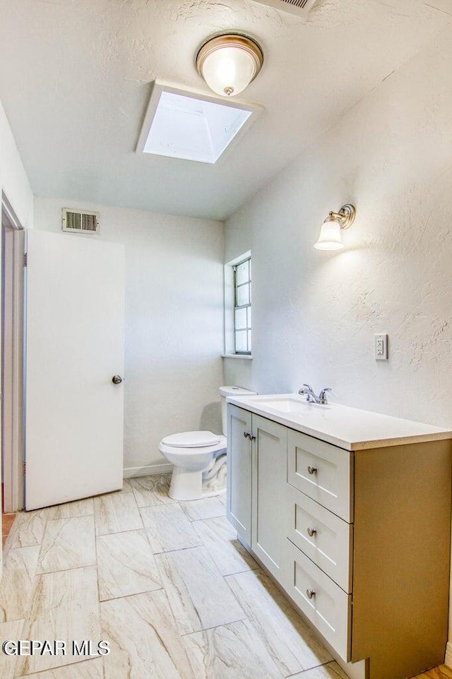 bathroom featuring toilet, vanity, and a skylight