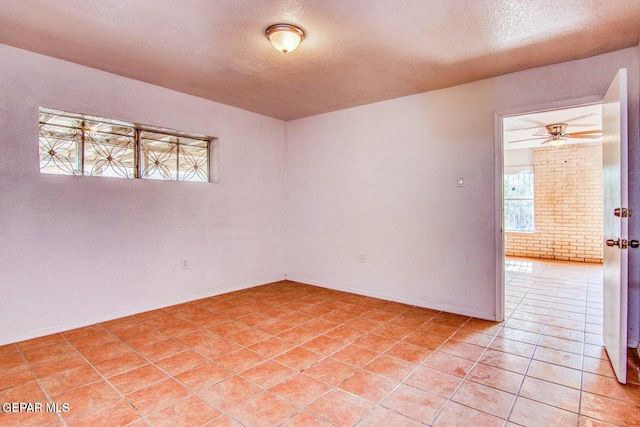 empty room with a textured ceiling, light tile patterned floors, and ceiling fan