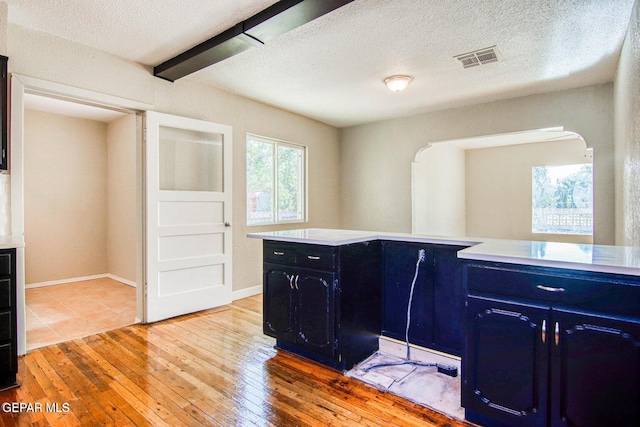 kitchen with a textured ceiling, beamed ceiling, and light wood-type flooring