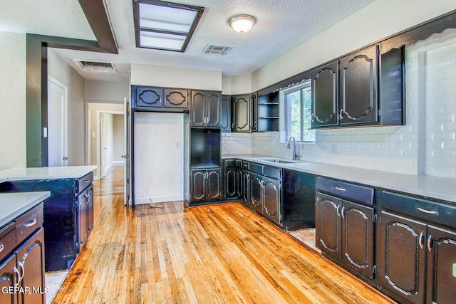 kitchen with sink, tasteful backsplash, a textured ceiling, light hardwood / wood-style floors, and a skylight