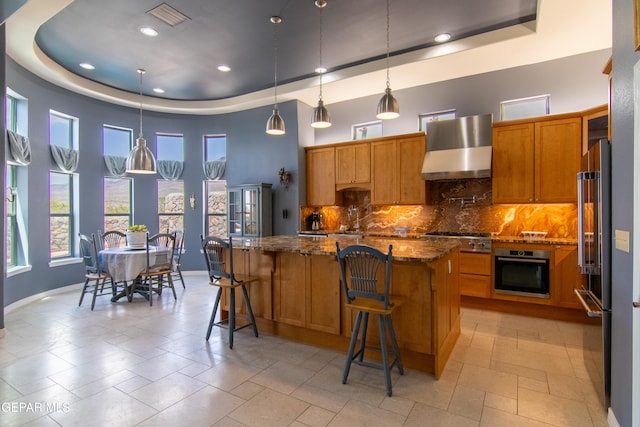 kitchen with a kitchen island, wall chimney range hood, a tray ceiling, and stainless steel appliances