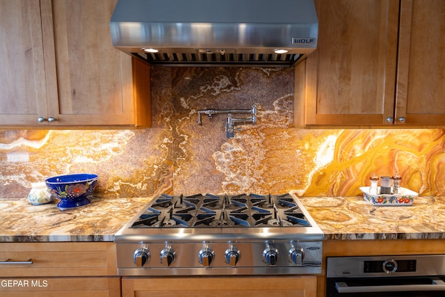 kitchen featuring stainless steel appliances, ventilation hood, light stone counters, and backsplash