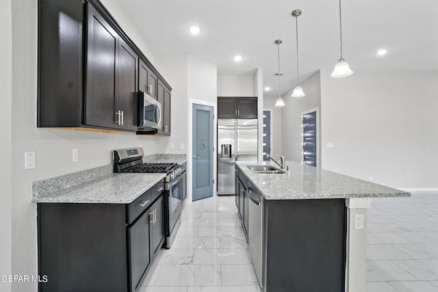 kitchen featuring a kitchen island with sink, hanging light fixtures, stainless steel appliances, sink, and light stone counters