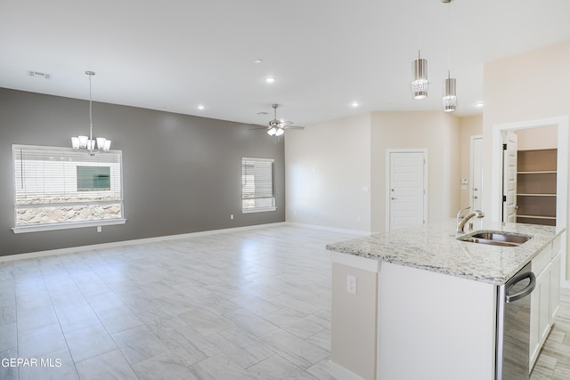 kitchen with light stone counters, an island with sink, white cabinetry, sink, and decorative light fixtures