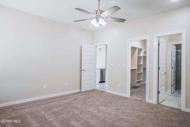 unfurnished bedroom featuring a closet, ceiling fan, light carpet, and a walk in closet