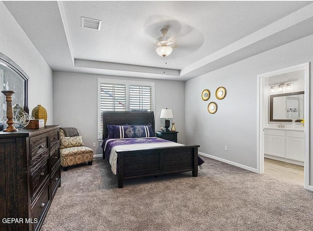 bedroom featuring ceiling fan, carpet flooring, ensuite bathroom, and a tray ceiling