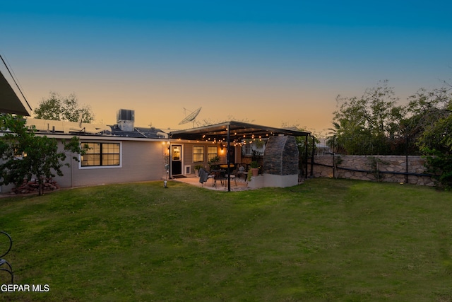 back house at dusk with a patio area and a yard