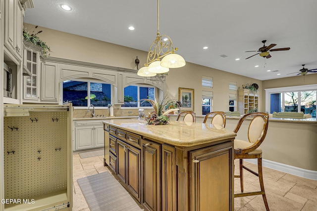 kitchen with hanging light fixtures, ceiling fan, a kitchen island, a breakfast bar, and light stone countertops