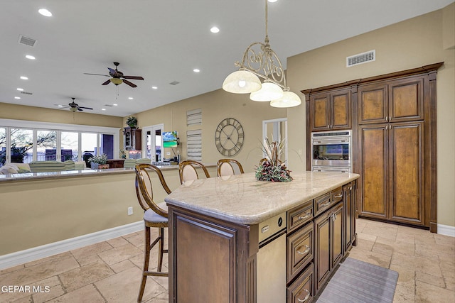 kitchen featuring a center island, a kitchen breakfast bar, ceiling fan, decorative light fixtures, and light stone counters