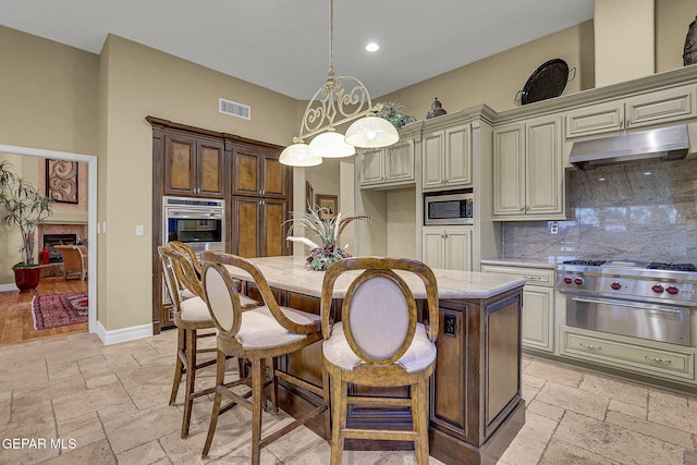 kitchen with cream cabinets, stainless steel appliances, light stone counters, and backsplash