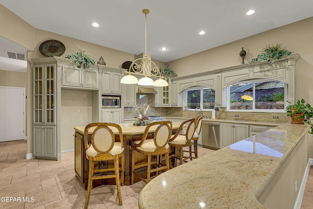 kitchen featuring cream cabinetry, hanging light fixtures, stainless steel appliances, light stone counters, and decorative backsplash