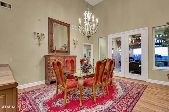 dining area featuring an inviting chandelier, french doors, a towering ceiling, and light wood-type flooring