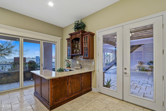 kitchen with decorative backsplash, french doors, kitchen peninsula, sink, and light stone counters