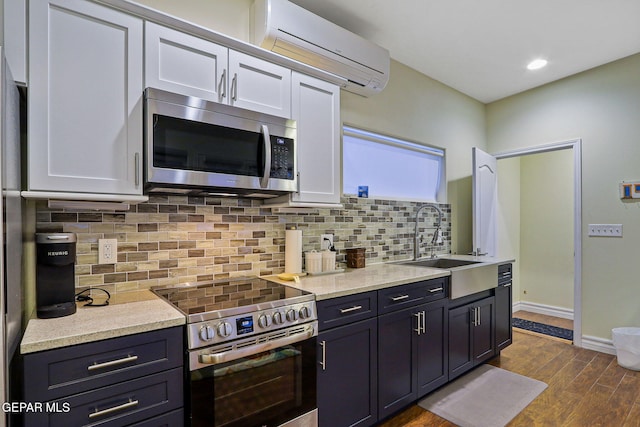 kitchen featuring a wall mounted AC, dark wood-type flooring, appliances with stainless steel finishes, and white cabinets