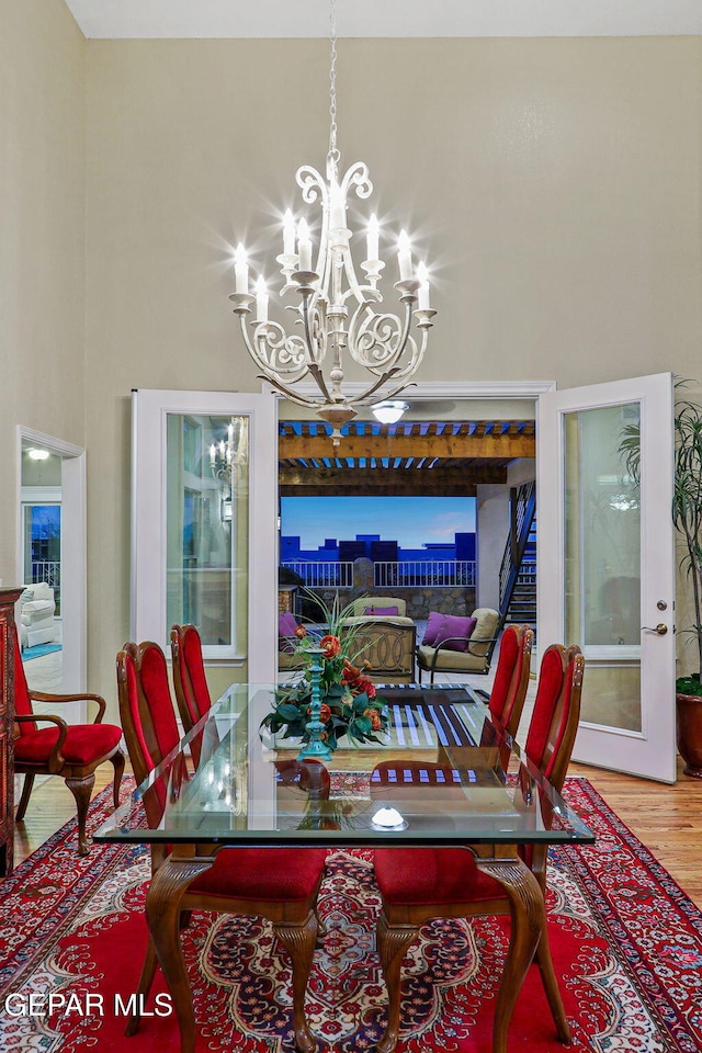 dining area with a towering ceiling, french doors, wood-type flooring, and an inviting chandelier