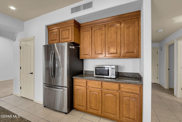 kitchen featuring dark stone countertops, stainless steel appliances, and light tile patterned flooring