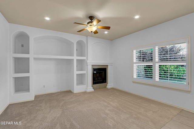 unfurnished living room featuring ceiling fan, light carpet, built in features, and a tile fireplace