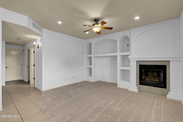 unfurnished living room featuring ceiling fan, light colored carpet, a tile fireplace, and built in shelves