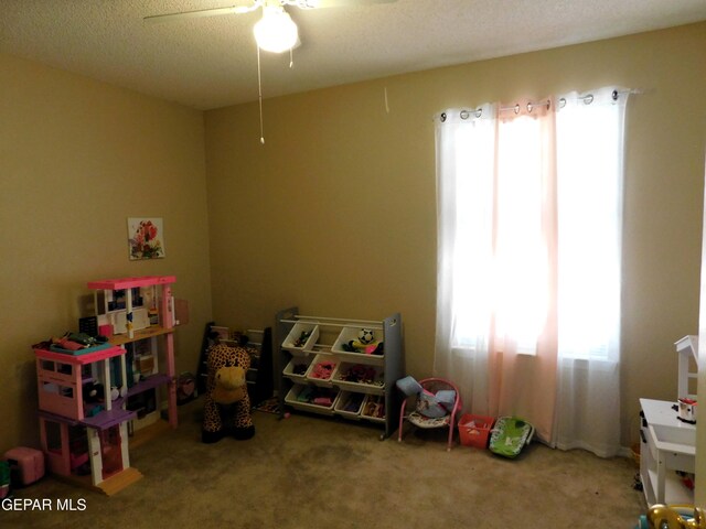 playroom with ceiling fan, a textured ceiling, carpet floors, and a healthy amount of sunlight