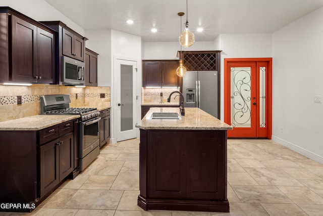 kitchen with hanging light fixtures, light stone counters, an island with sink, appliances with stainless steel finishes, and sink