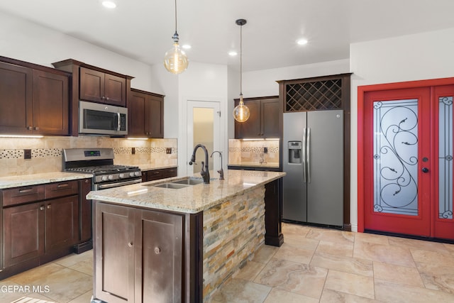 kitchen featuring decorative backsplash, a kitchen island with sink, hanging light fixtures, sink, and appliances with stainless steel finishes