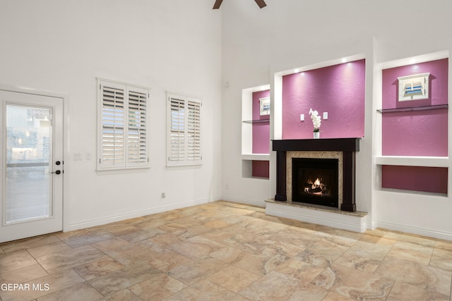 unfurnished living room with a towering ceiling, ceiling fan, built in features, and a premium fireplace